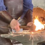 6.5 - The sparks get my immediate attention and together with the hammer and the two arms, form good leading lines to the point of action. The bright white area in the furnace is a big distraction and should be darkened. I also see that the man's arms and hands and the hammer are not in sharp focus.